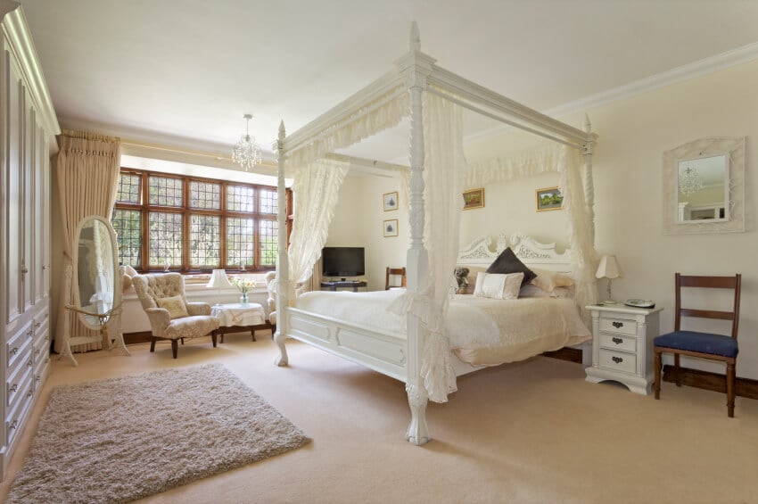 这间传统与现代结合的主卧室的焦点是带有蕾丝窗帘和帷幔的华丽雕花天篷床。所有需要的存储都包含在一堵内置的墙内。