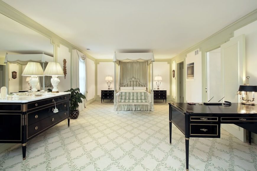 宽敞的主卧室，可爱的树叶图案地毯排列在钻石图案。光滑的黑色家具与传统的白色顶篷床形成鲜明对比。天篷上装饰着金色的小流苏。