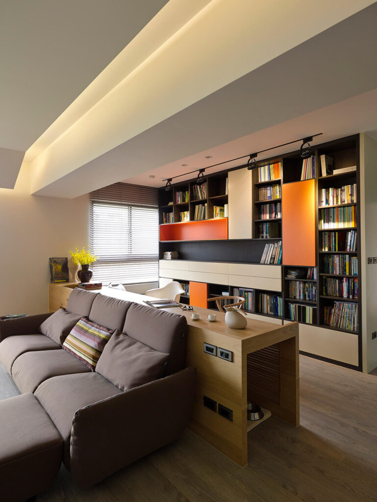 书桌的设计清晰地将家庭办公室与客厅分隔开来。在这里，我们可以近距离看到巨大的墙壁大小的书架，上面镶着橙色的镶板。