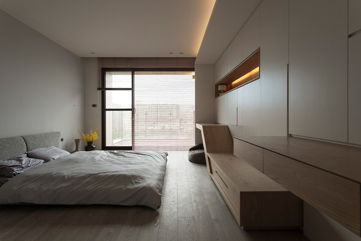 当代风格的主卧室有一张灰色的落地床，面对着内置的木制货架和储物柜。