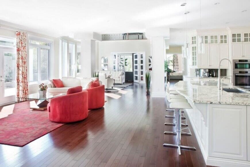 客厅区域大胆的红色有助于在视觉上将其与豪华的白色大理石厨房区分开来，同时仍然允许光线通过玻璃门和宽敞的窗户进入厨房区域。