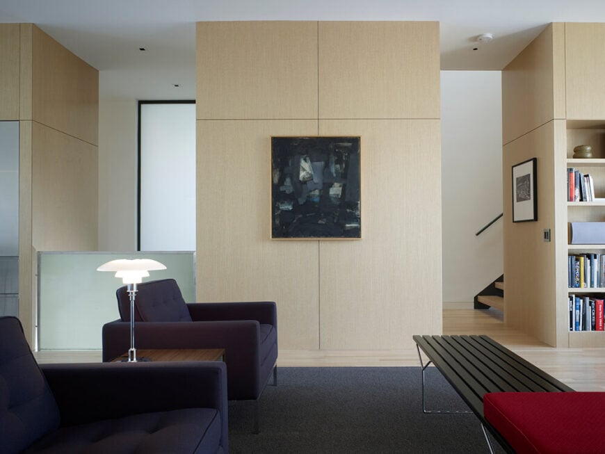 在这里，我们看到了客厅，更轻的木墙板与一套定制的现代家具相结合。一对棱角分明的深蓝色俱乐部椅正对着木制和钢制的长凳，周围环绕着现代主义的细节。