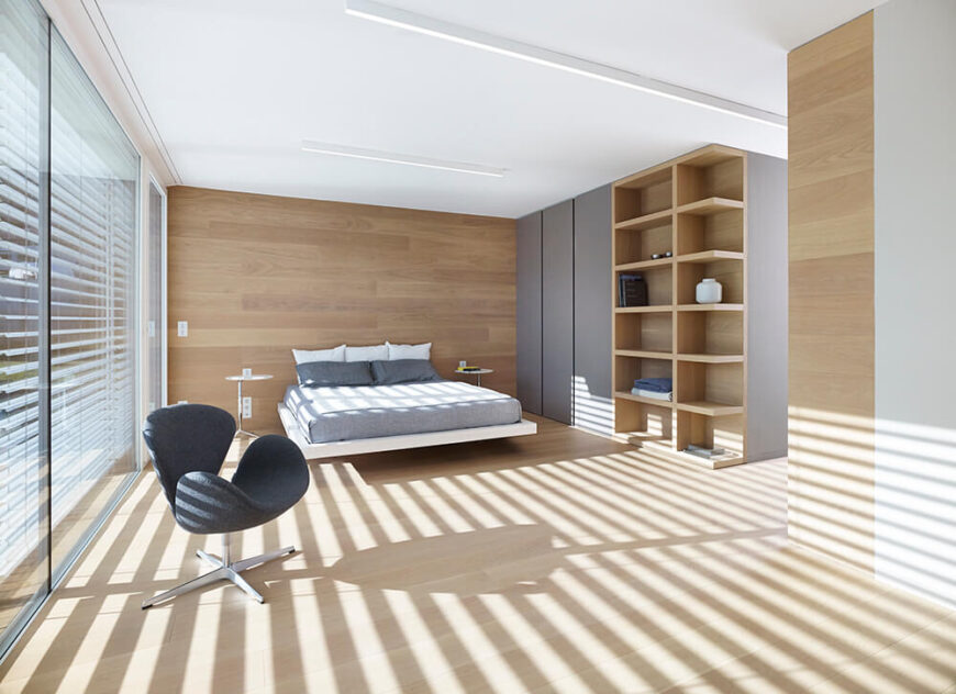 主卧室和家里的其他房间一样宽敞，以书架和极简主义的灰色储藏室为特色。床后墙上深色的木头起到了微妙的强调作用。