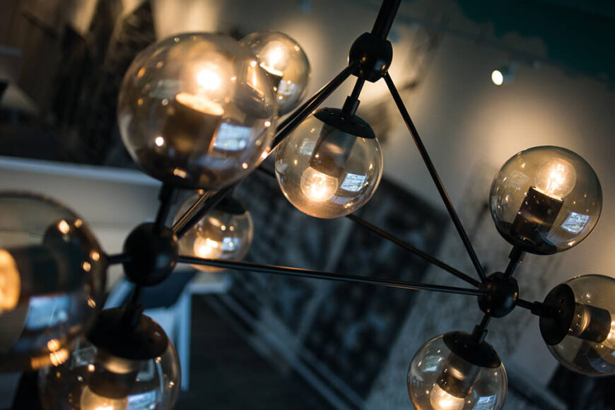 照明包括这样的枝形吊灯，以一组相互连接的烟熏球体和黑色金属管道为特色。它颠覆了传统意义上的吊灯。
