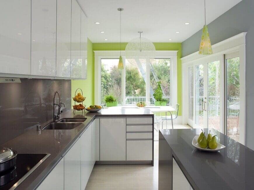 白色、灰色和亮绿色的配色方案将这个厨房与其他相同的当代风格区分开来，并使明亮的白色橱柜不会压倒房间的其余部分。整个厨房都保持橱柜和柜台的高光泽度，有助于将大窗户的光线反射到房间深处。