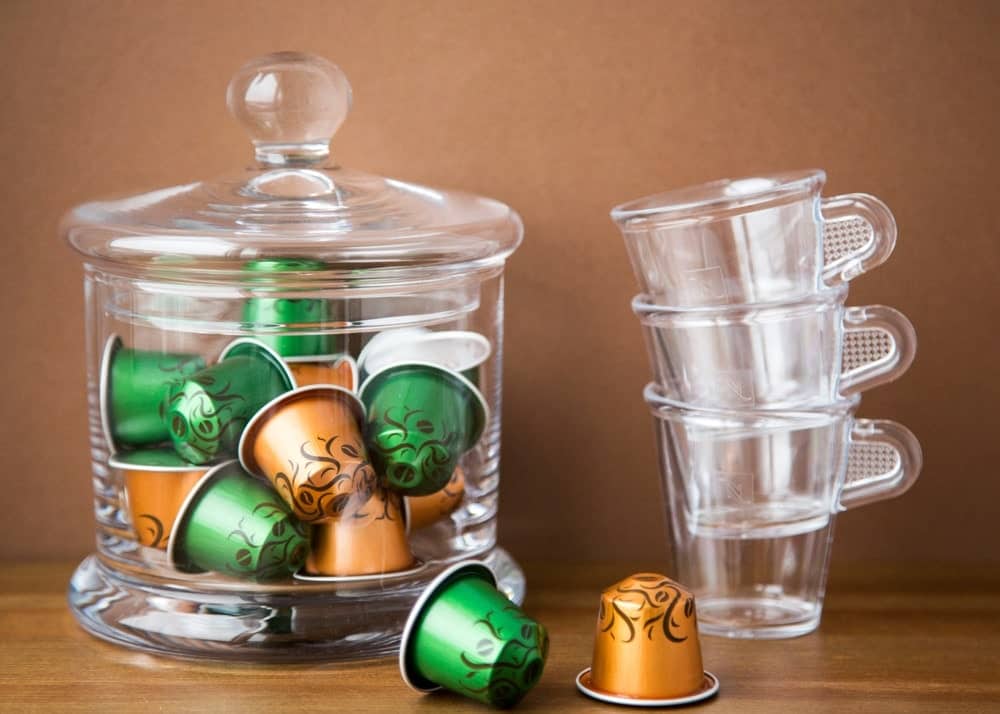 一个玻璃容器里的k杯和一堆玻璃咖啡杯，旁边是木桌上的几个k杯。