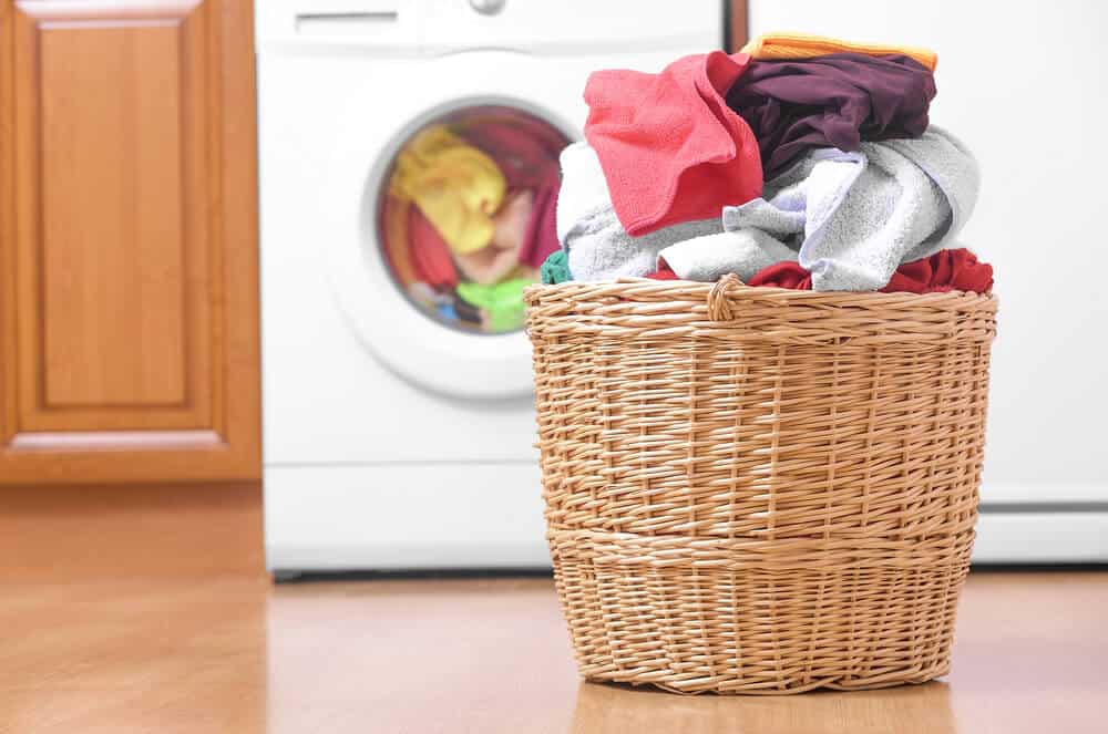 装满衣物的洗衣篮放在洗衣机前面。