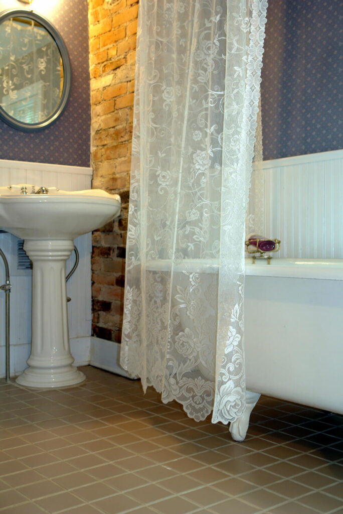 这个小浴室空间的一角以砖代替墙纸为特色。由于天花板上悬挂着优雅的窗帘，爪形浴缸有了额外的隐私选择。