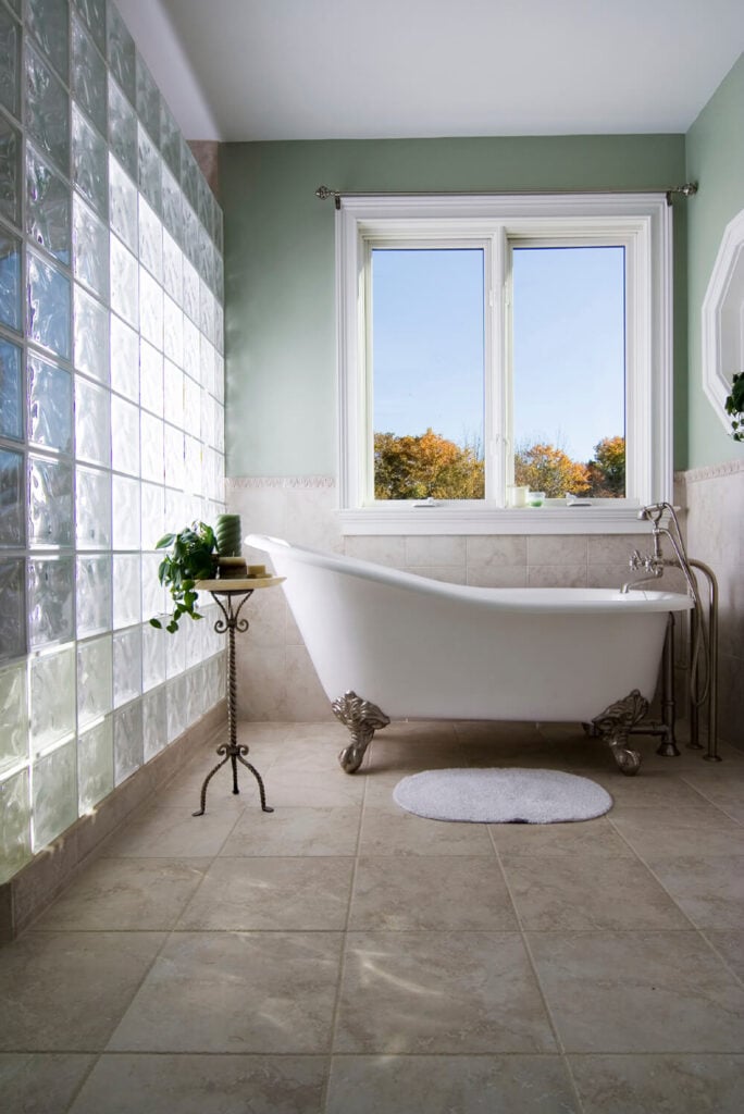大的方形瓷砖在浴室的墙壁上延伸到一半，作为浴缸的后挡板。玻璃砖墙是浴室的特色，可以让充足的自然光洒进房间。