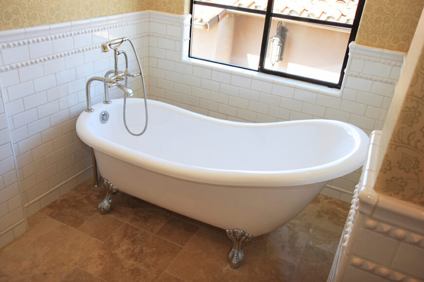 这个爪形浴缸坐落在纹理瓷砖上，正位于窗户下方。这个空间自然采光很好，白色瓷砖沿着墙延伸到一半，作为浴缸区域的后挡板。