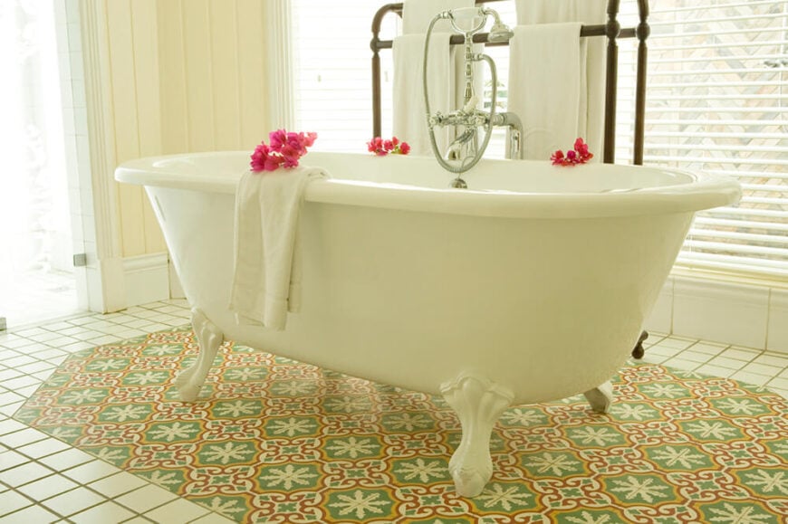这个巨大的爪足浴缸坐落在一块重音瓷砖的中心，与周围的地板有不同的设计模式。浴缸周围的窗户为房间提供了自然采光。