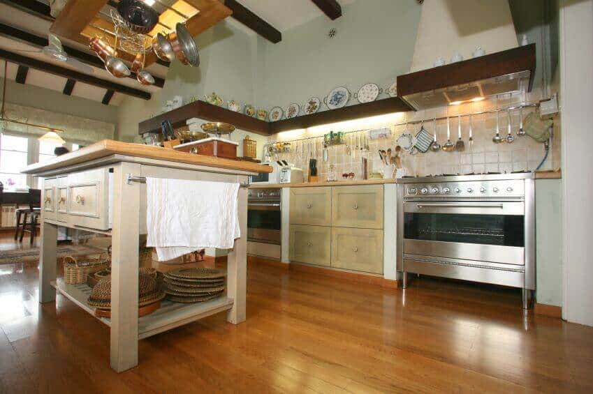 这个锅架兼作古色古香的小屋厨房的厨房岛上的灯具。选择浅色木材，而不是与房间其他部分的深色木材相匹配，有助于保持锅架在房间中心看起来不笨重。