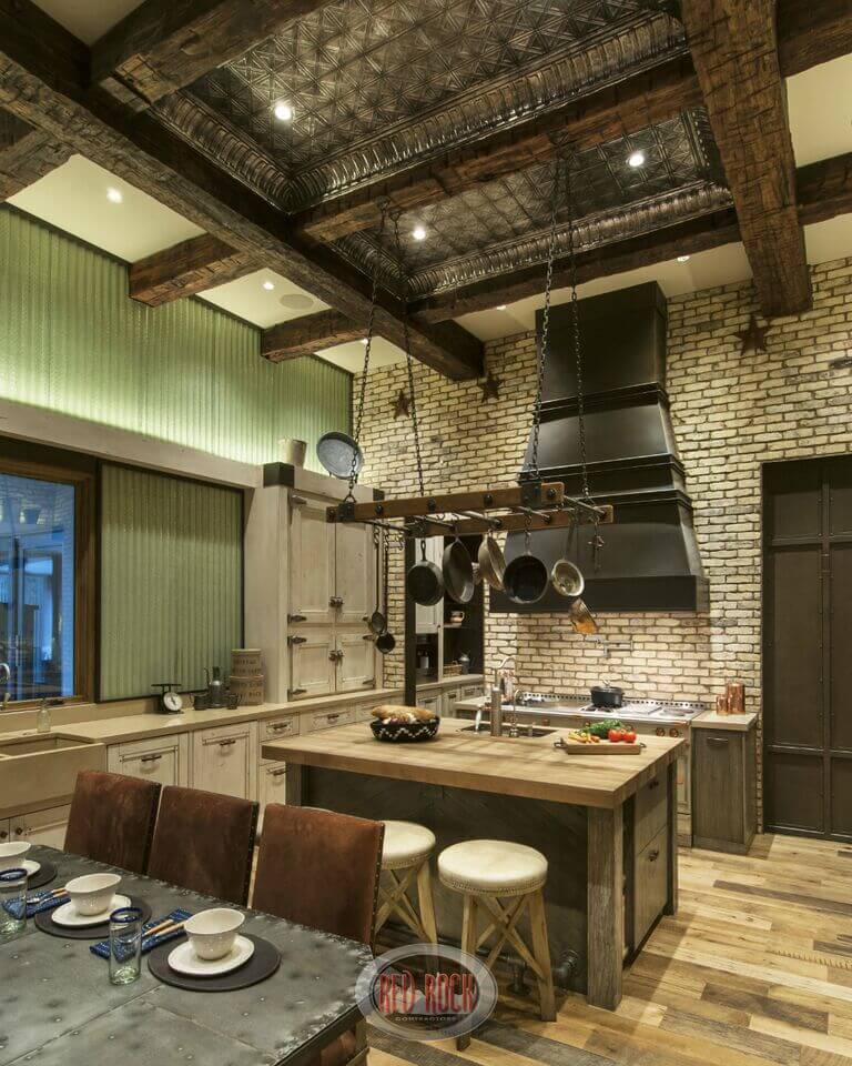 一个质朴的石头和金属厨房，一个小的木制就餐岛台，在准备空间和水槽上方有一个锅架。