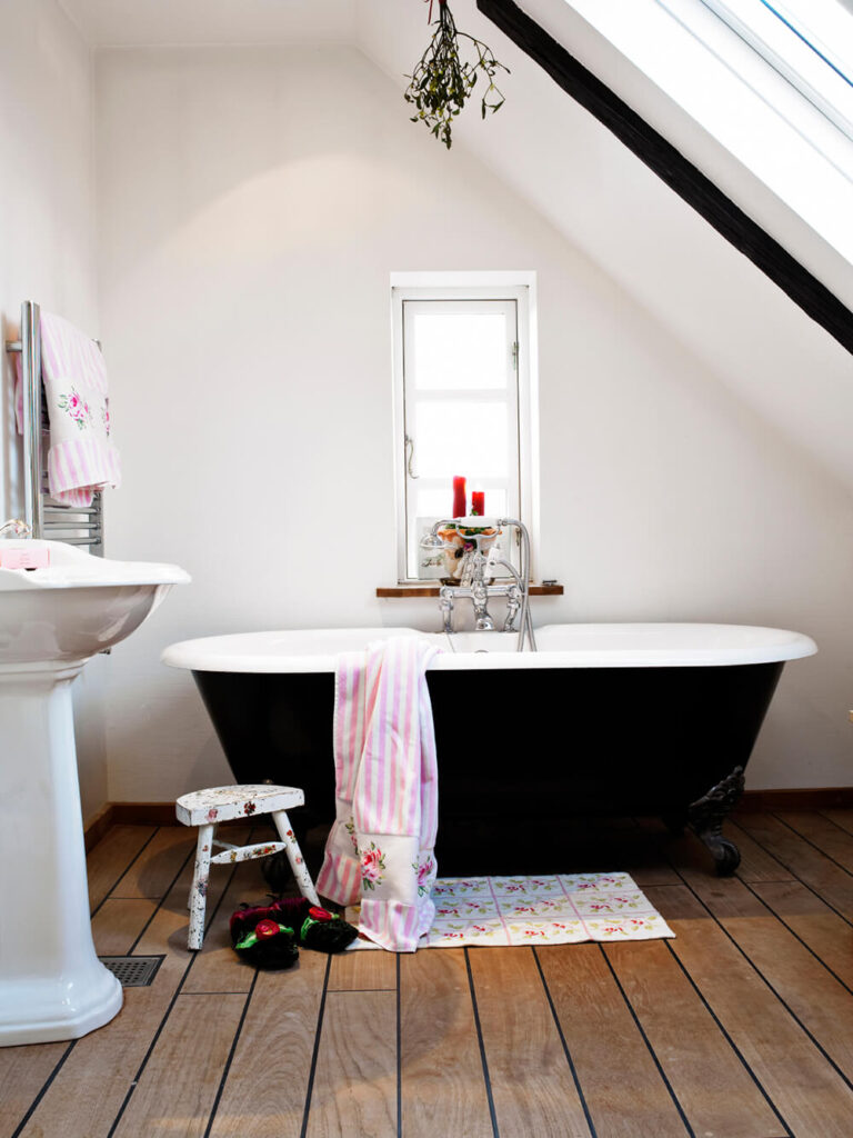 这是一个简单而朴素的空间，浴室的特色是一个黑色的爪足浴缸，坐落在明确的木纹地板上。在这个小的浴室空间里，一个陶瓷底座水槽位于旁边，与浴缸一起。