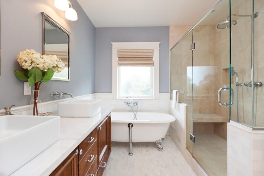 一个巨大的玻璃墙淋浴器位于浴室的一侧，占据了相当大的空间。爪形浴缸被塞在浴室的柜台和淋浴间，就在一扇明亮的窗户下面。