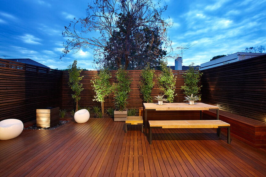 庭院是极简主义风格的体现，奢华的木地板和私密的围栏包裹着整个空间，点缀着修剪整齐的植物。新颖的白色豆椅和传统的野餐桌构成了一个真正有用的空间。