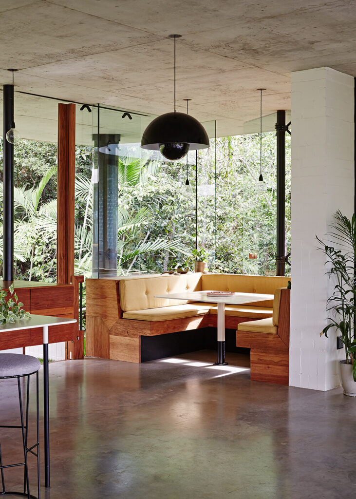 在一个全玻璃框架的角落里，一个丰富的木制早餐角温暖了这个空间。天然材料与明亮的白色墙壁和混凝土地板形成了强烈的对比。
