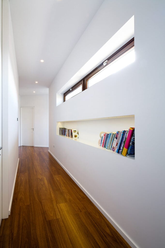 沿着大厅走到家里更私密的地方，我们看到一个有用的内置书架，它映出了上面窗户的样子。原始的白色环境被天然硬木地板的丰富色调所固定。