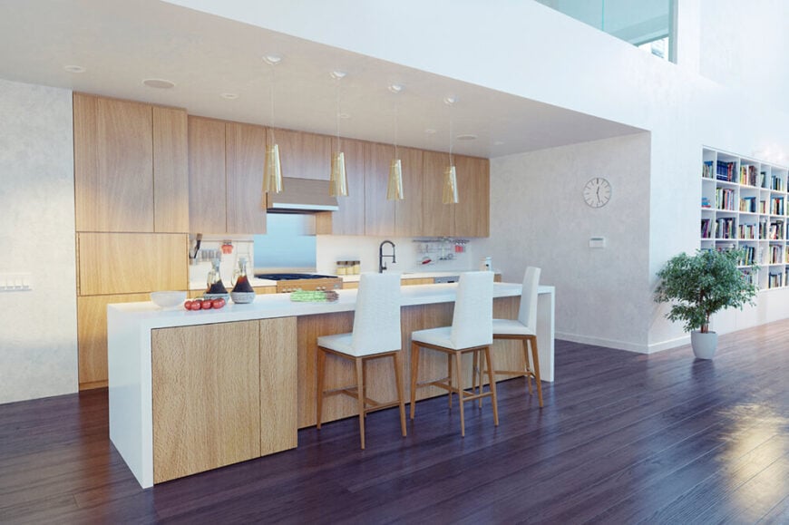 一个可爱的极简主义白色和自然的轻木厨房，对比鲜明的深色硬木地板。厨房区域位于大型开放式主要起居区的凹室下方。