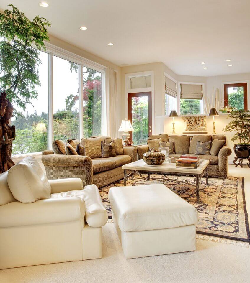 在这个传统的客厅里，我们看到了质感的棕色沙发和大胆的白色皮革扶手椅，前景中有配套的软脚凳。通过一组环绕式的窗户，整个房间都散发着白色的光芒。
