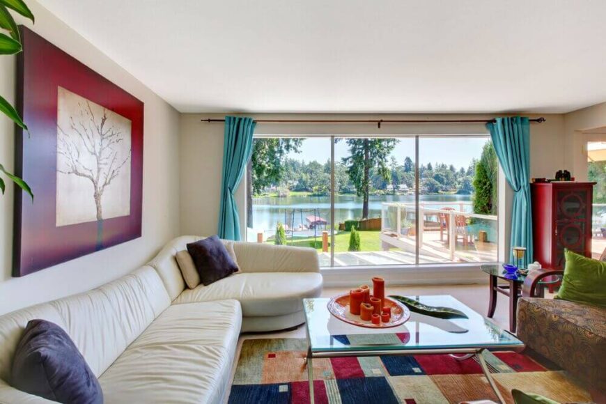 这座湖边的住宅拥有巨大的窗户，可以欣赏广阔的水上景观，并允许充足的自然光进入室内。一条长长的白色皮革组合家具将彩色空间包裹在有图案的区域地毯上。