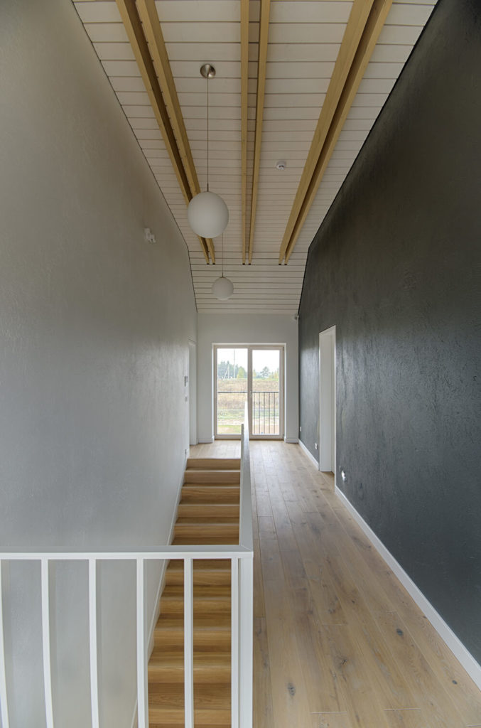 从楼梯的顶部可以看到白垩色的硬木地板和纹理墙。与房屋外部相似的木镶板覆盖了天花板，有垂坠的球体照明和金色的木椽子。