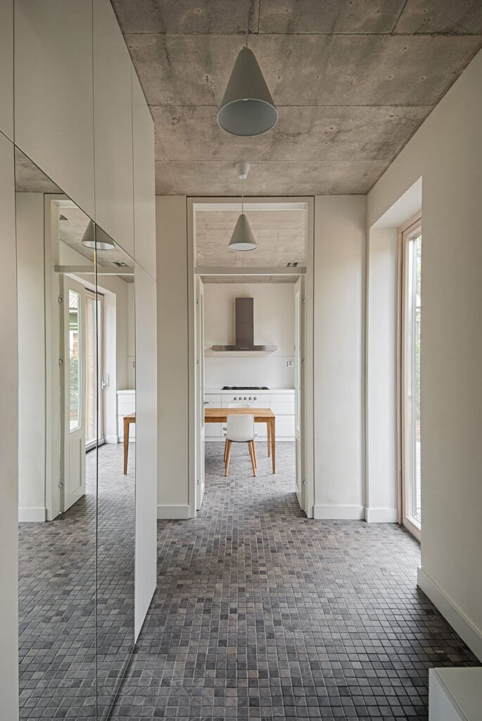 这条室内走廊通向厨房。镜子有助于将光线从通往甲板的滑动门反射到大厅。混凝土天花板是调节温度和在温暖的月份保持房子凉爽的好选择。华丽的瓷砖地板抵消了苍白的墙壁，并将苍白的混凝土与配色方案联系起来。
