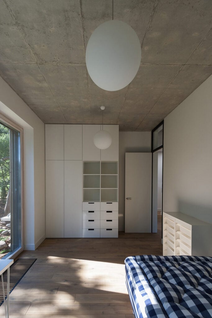 这是两间客卧中的一间，可以看到院子，并提供了大量的内置存储空间。浅色的木地板与白色的墙壁和储藏室形成了平衡。大型球形吊灯悬挂在水泥天花板上。