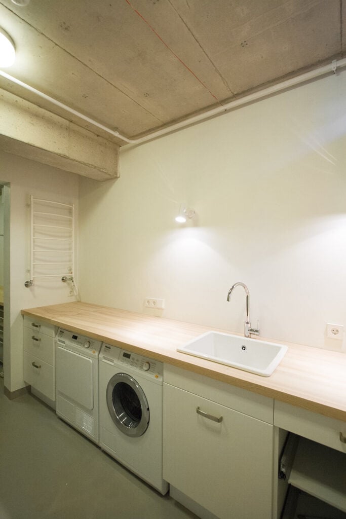 洗衣房也在二楼，设有一个长长的木质台面和白色橱柜。混凝土天花板也出现在这个房间里。
