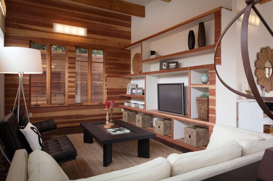 在开放区域的另一端，我们看到客厅装饰着天然木材和优雅的当代家具。墙上的一组复杂的内置搁架为艺术和存储提供了空间，而左边的全木特色墙则在家中延续了这一元素。