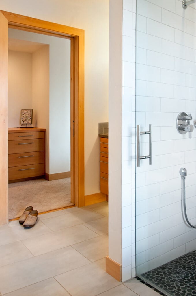 主浴室设有一个玻璃封闭式步入式淋浴房，白色瓷砖墙，材料的变化，同时保持整个家庭使用相同的调色板作为风格的结缔组织。