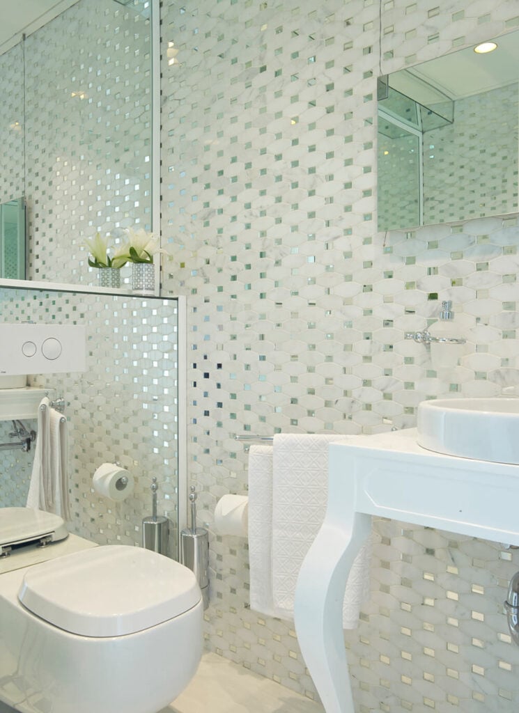 这是家里的一间浴室，这是一个使用镜子来扩大视觉尺寸的小空间。白色的梳妆台，带水槽，靠在右边极富质感的墙壁上。