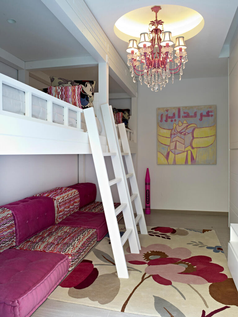 这个儿童房是一个梦幻般的，有趣的空间，色调相对保守。在左边，一对阁楼床悬挂在一个巨大的部分上，白色的梯子立在一个枝形吊灯下面。一张简单的花卉地毯占据了空间的中心，远处的墙上挂着一幅与之相配的彩色油画。