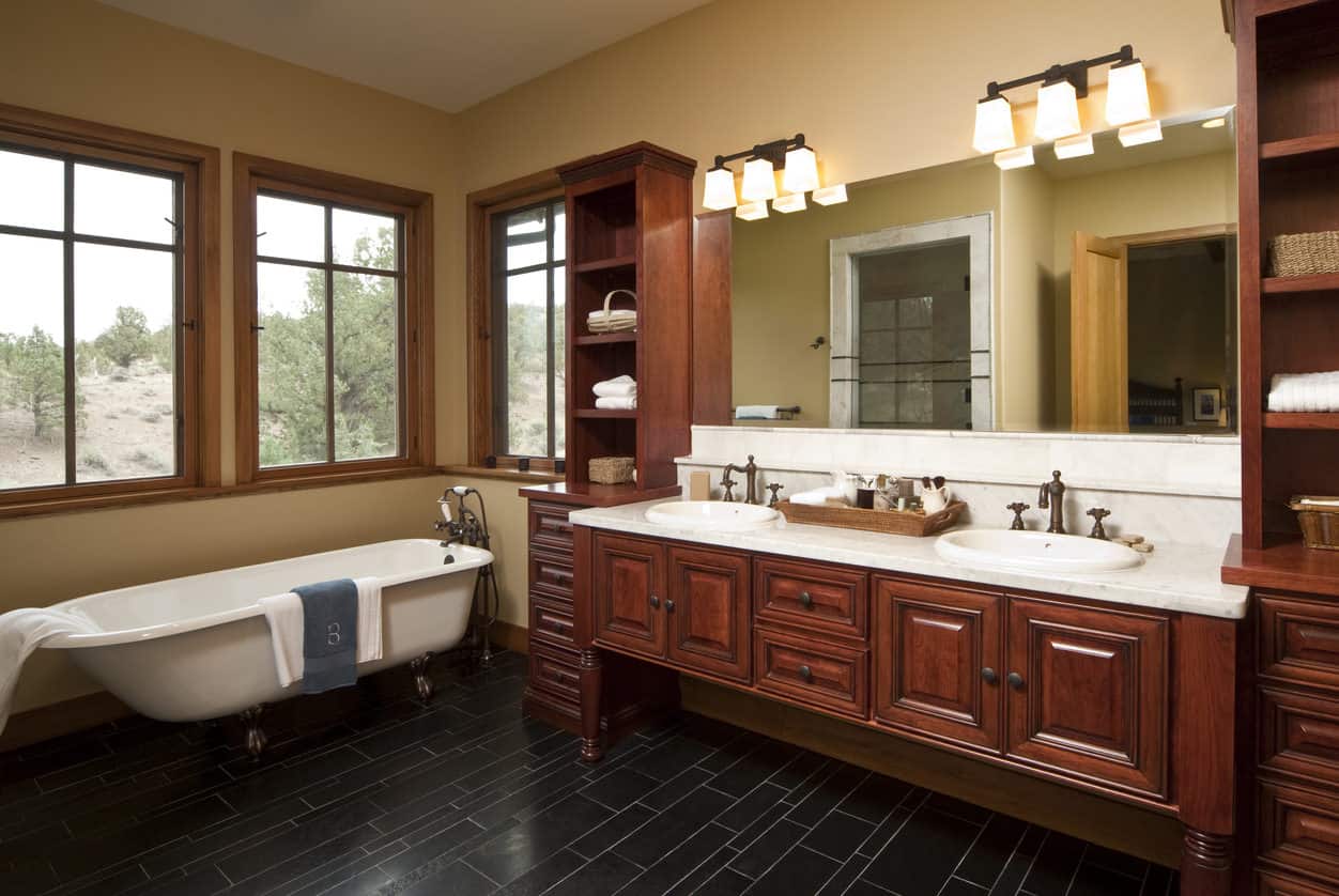 宽敞明亮的主浴室，白色爪足浴缸被窗户包围，旁边是一个大型内置双水槽梳妆台。