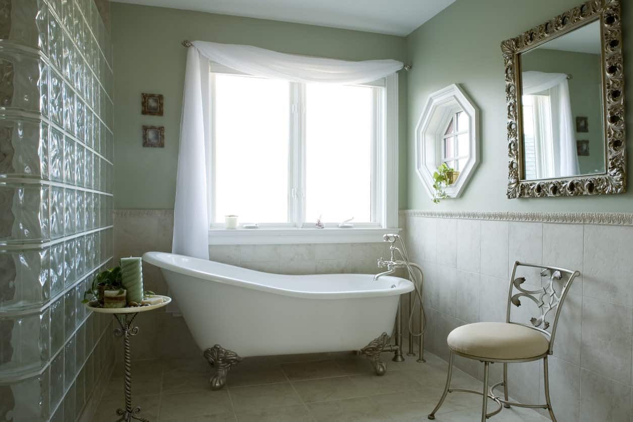 绿色主浴室与大爪足浴缸凹区，椅子，桌子和窗户。