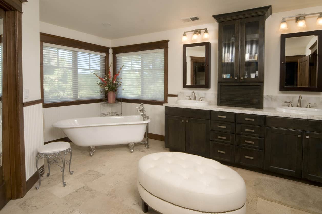 宽敞的主浴室角落里有一个古董爪足浴缸，暗木梳妆台和椭圆形的白色簇绒搁脚凳。