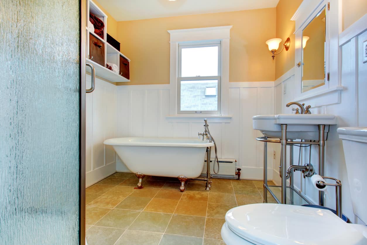 黄色和白色的主浴室，米黄色瓷砖地板上有一个旧的爪形浴缸。