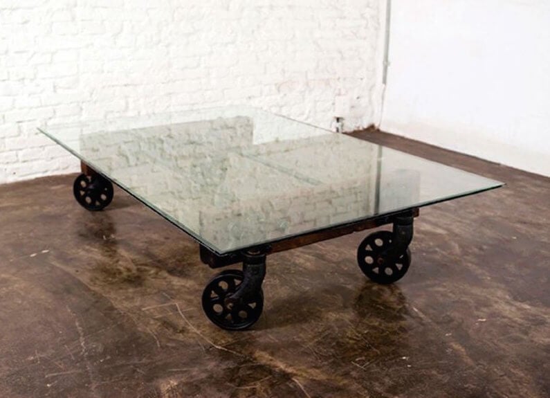 在工业推车设计的灵感扭曲中，我们看到这张桌子的经典支撑支撑着光滑的玻璃面板，而不是原来的木质结构。这创造了一个现代和工业风格的有趣混合，以及一个完全独特的咖啡桌。