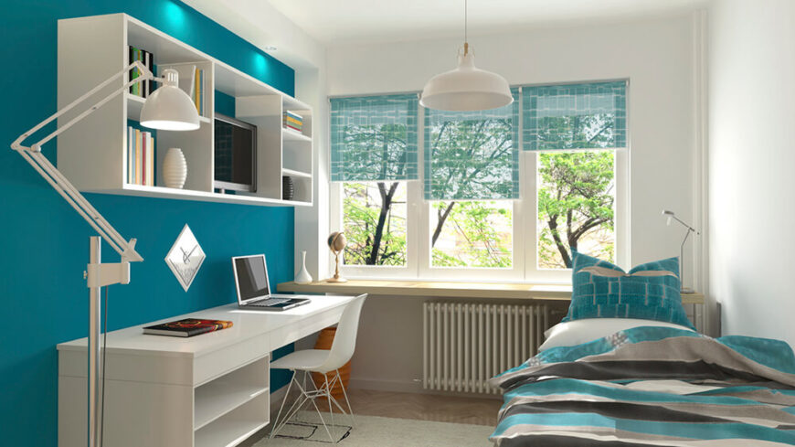 干净的白色墙壁和办公桌区域，大胆的蓝色强调墙有助于平衡配色方案。透明的窗帘和床上用品也有帮助。书桌上方的置物架提供了额外的存储空间和装饰。这个空间有宿舍的感觉，非常适合单身人士。