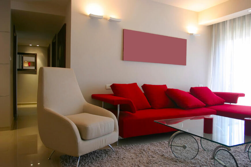 这间客厅铺着光滑的瓷砖地板，一块宽大的长毛绒地毯将所有家具聚集在一起。红色沙发充满活力，与空间其他部分的米色形成对比。