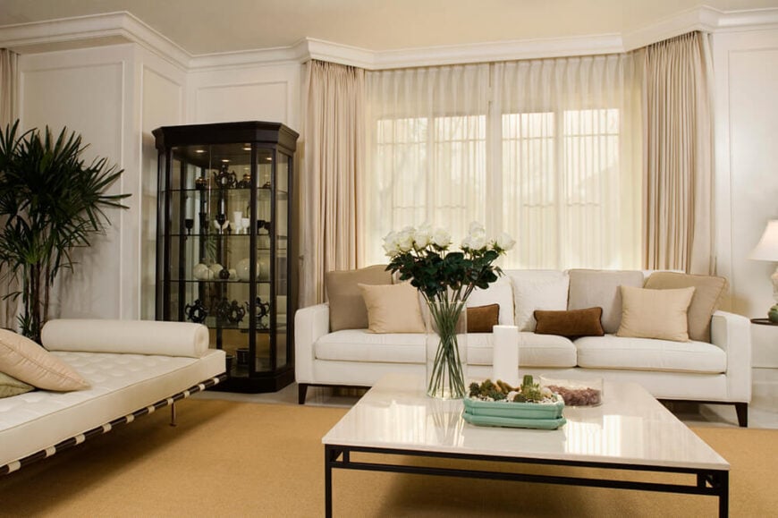 大面积的棕褐色地毯铺在光滑的大理石地板上，有助于将房间里的家具聚集在一起。角落里放着一个瓷器柜，黑色的框架与房间里的浅色形成了强烈的对比。