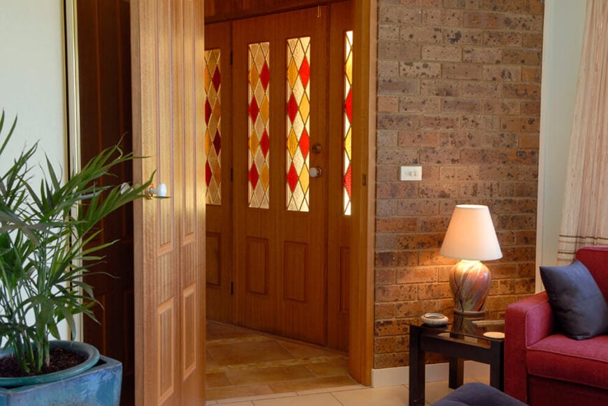 这个入口以丰富的彩色木门为特色，在拐角处过渡到红砖。门上的彩色玻璃板保持了入口通道的低光，并补充了丰富的木材色调。