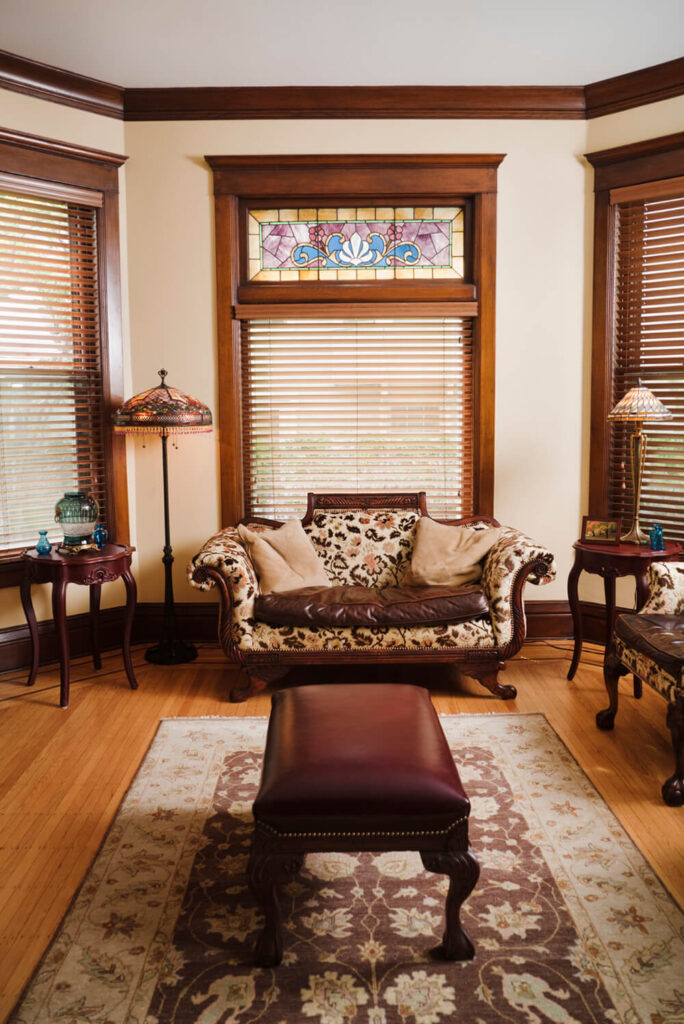 浅色的硬木地板与房间窗户周围的染色木装饰相匹配。窗户上方的一段彩色玻璃赋予了房间的特色，并与家具和地毯的设计相呼应。