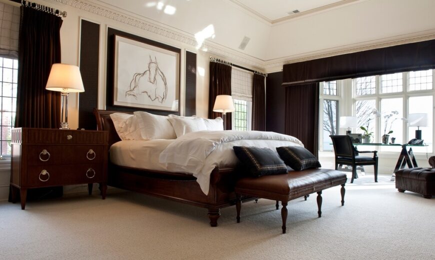 这间大卧室有一个高高的拱形天花板，床周围有足够的空间。家具由丰富的染色木材和深色皮革组成，显示出富裕的地位。浅色的地毯和墙壁有助于与深色家具形成对比，而大窗户为书桌空间提供了充足的自然光线。窗帘的特色是帮助将工作空间与卧室分开。