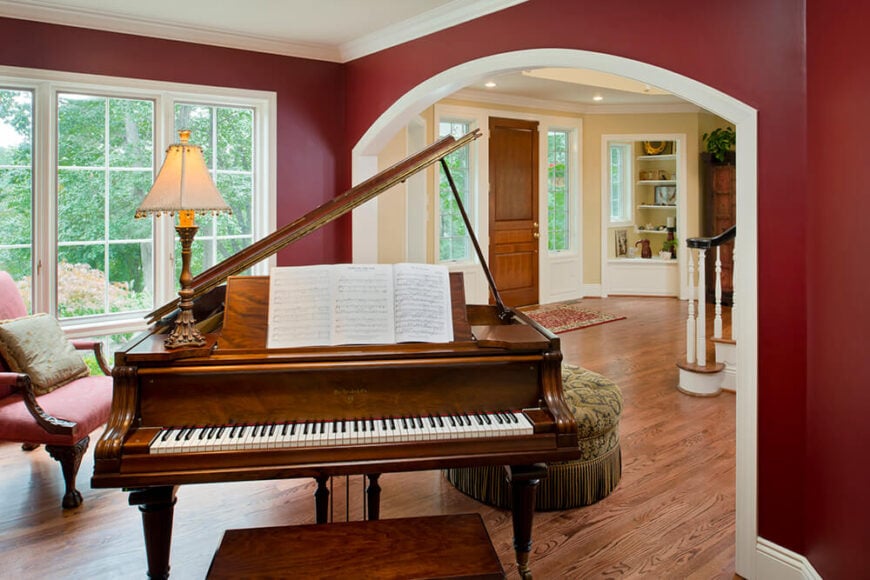 前面有一间带三角钢琴的客厅，可以看到后院的门厅。他们将新安装的木地板与现有的木地板相匹配，让整个房子都能流动起来。