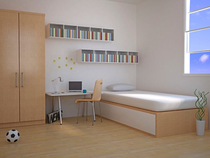 这间极简主义风格的卧室设有一张床、一张桌子、一个衣柜，以及床头和书桌上方的小架子单元。床脚附近有一扇窗户，可以让一些自然光照进来。床架、衣柜和桌椅都由轻木制成，与白色房间的其他部分相得益彰。