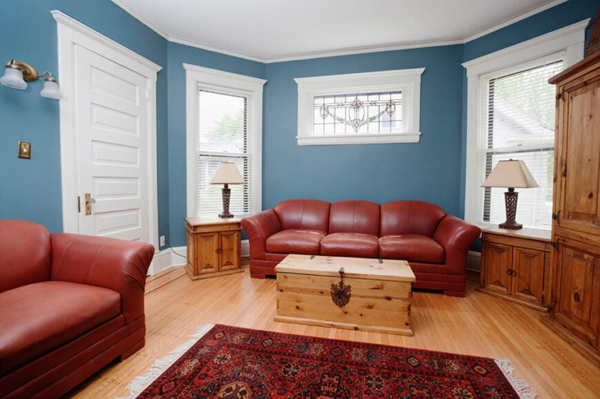 这间客厅铺着硬木地板，上面铺着一块设计复杂的小地毯。家具是皮革的，和地毯的颜色很相配。大沙发上方，有一扇设计优雅的彩色玻璃窗。