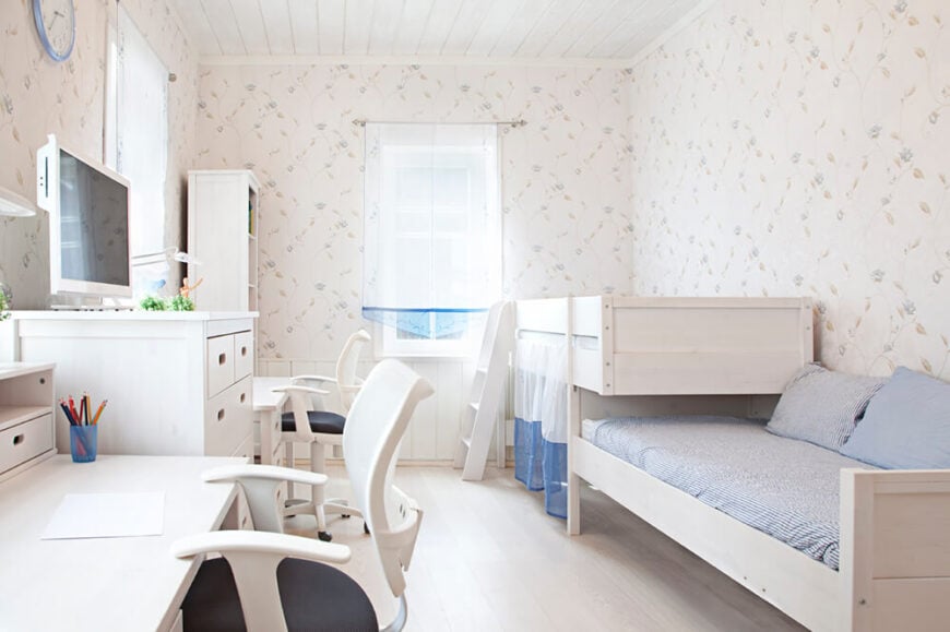 这个空间主要是白色的，墙上有微妙的图案，浅蓝色的被褥平衡了其他单色的主题。在两张床的对面，有两张桌子，中间是一组高高的抽屉和一台电视机。白色硬木地板是独特的，有助于房间的白色主题。