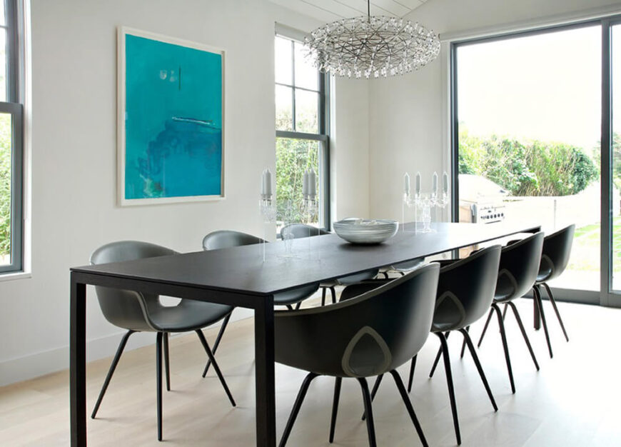 这个家的用餐区以优雅的透明烛台为特色，不会切断坐在桌子对面的人之间的任何互动。桌子本身又长又光滑，搭配的椅子是现代风格。一个独特的吊灯悬挂在这个空间的正上方，充满活力的艺术品有助于对比空间的颜色。