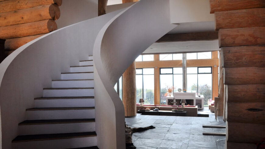 弯曲的楼梯漂浮在白色的开放空间上，定义了上层的外观，与土色的一楼截然不同。再往前，我们看到客厅在一组巨大的窗户下伸展开来。